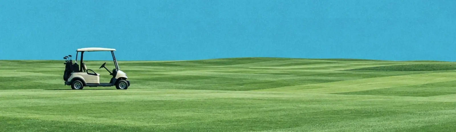 A golf cart parked on an open fairway under a clear sky